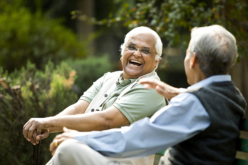 Two senior aged men sitting and laughing on bench